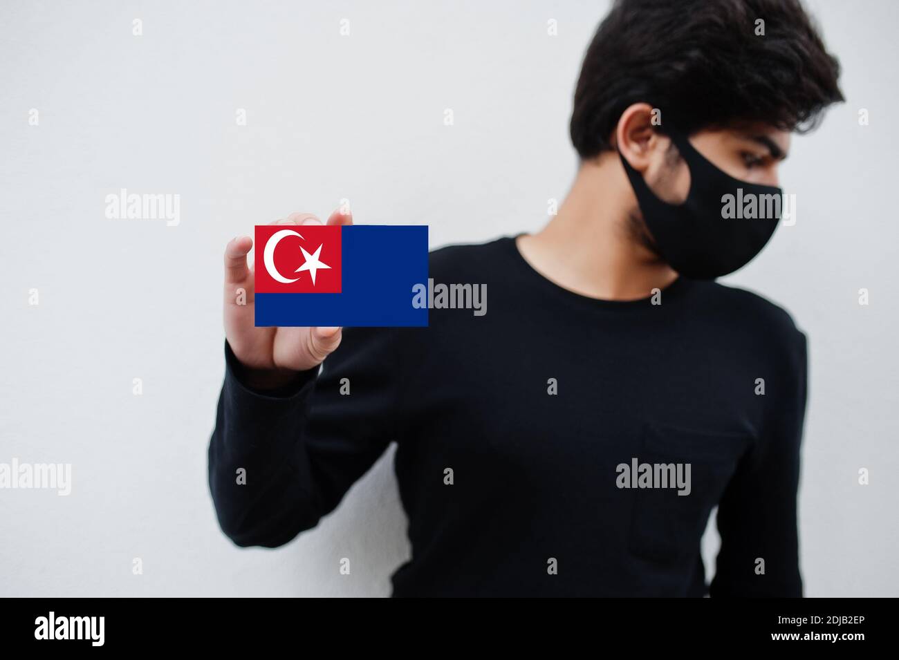 Malaiischer Mann tragen ganz schwarz mit Gesichtsmaske halten Johor Flagge in der Hand isoliert auf weißem Hintergrund. Staaten und Bundesgebiete von Malaysia Coronavirus c Stockfoto