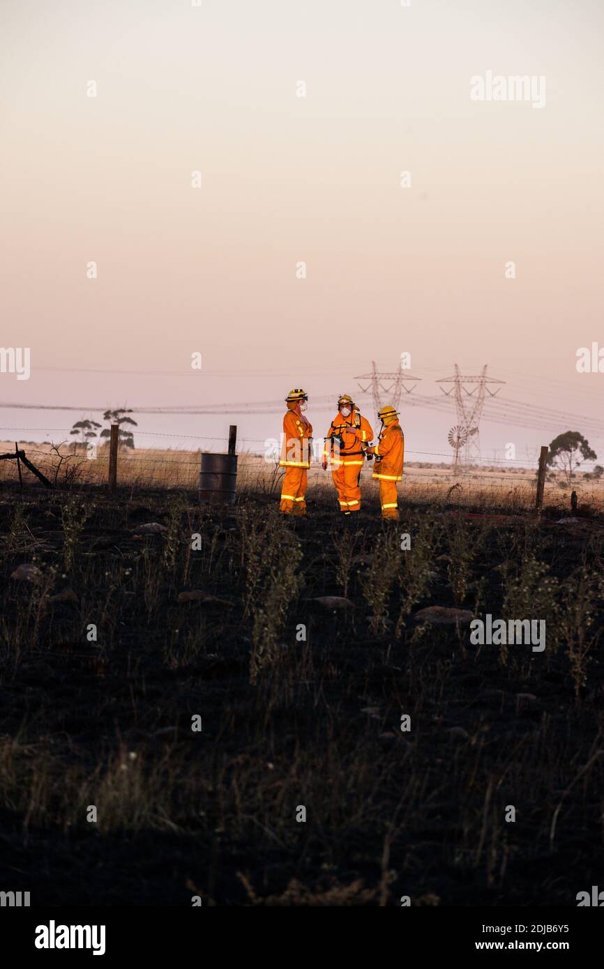 Melbourne, Australien 14 Dec 2020, Feuerwehrleute der County Fire Authority stehen auf dem geschwärztem Boden an der Stelle eines großen Grases in der Nähe von Mount Cottrell. Die Feuerwehr hat mit Flugzeugen und Feuerwehrmannschaften einen 110 Hektar großen Grasbrand im äußersten Westen Melbournes kontrolliert, der mehrere Schuppen und Autos zerstört. Stockfoto