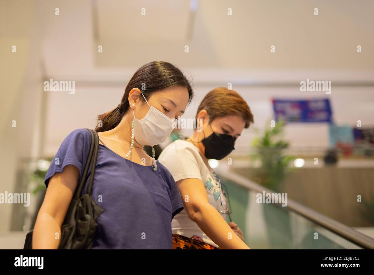 Asiatische Frauen in Schutzmaske stehen auf Rolltreppe im Einkaufszentrum. Stockfoto