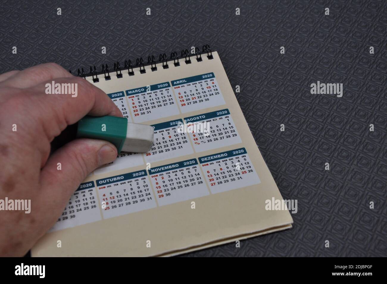Hand eines Mannes mit einem Gummi Radieren eines Kalenders 2020, auf einem schwarzen geometrischen Hintergrund, ein schwieriges Jahr, in dem nichts getan oder produziert wurde Stockfoto