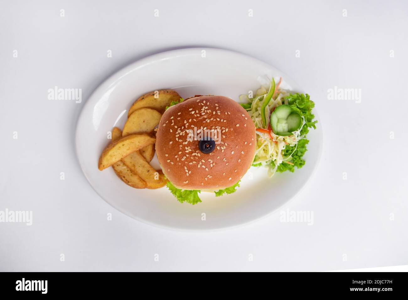 burger auf einem Teller mit Sesamkörnern auf einem weißen Teller. Draufsicht auf Burger und Kartoffelkeile mit Gemüse auf weißem Hintergrund Stockfoto