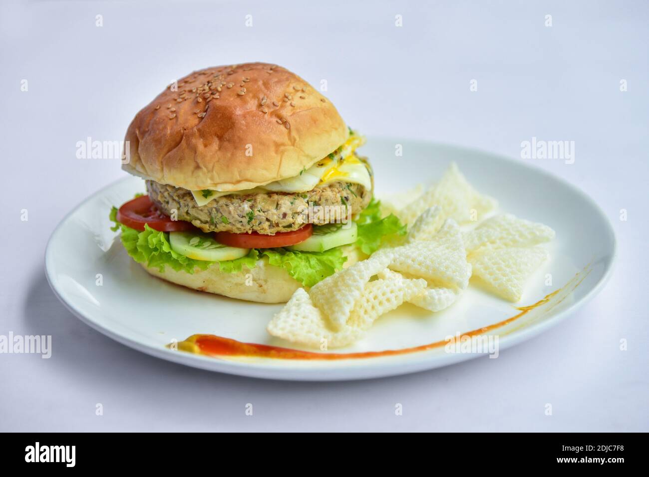 burger auf einem Teller mit Chips. burger mit Patty und Gemüse wie Gurken, Tomaten, Salat und halb gekochten Ei und Chips. Stockfoto