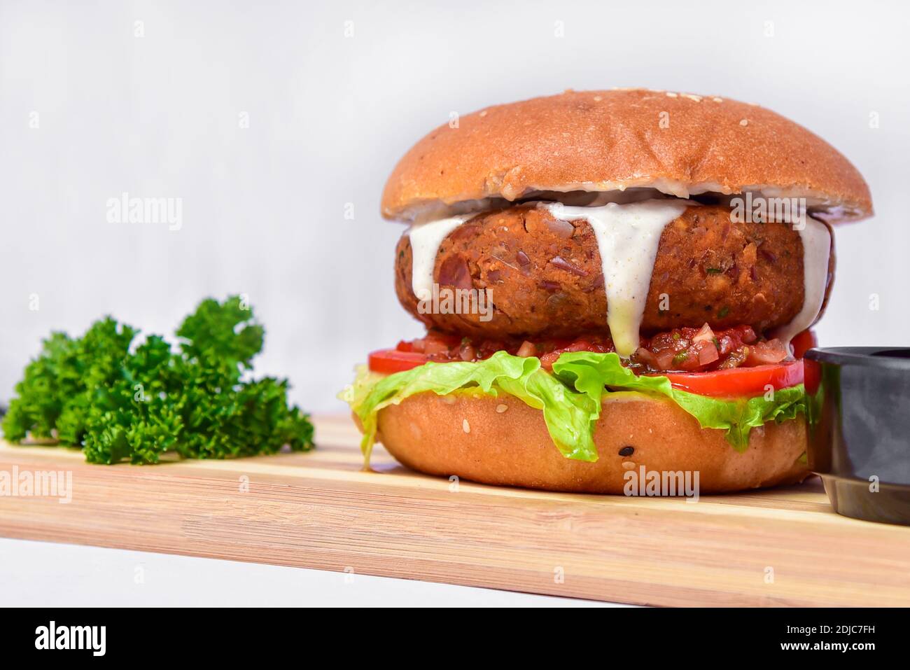 Saftiger Burger mit großem Patty und darauf tropfender Mayonnaise. Fleisch und Gemüse in einem Burger Augenhöhe Foto auf weißem Hintergrund. Stockfoto