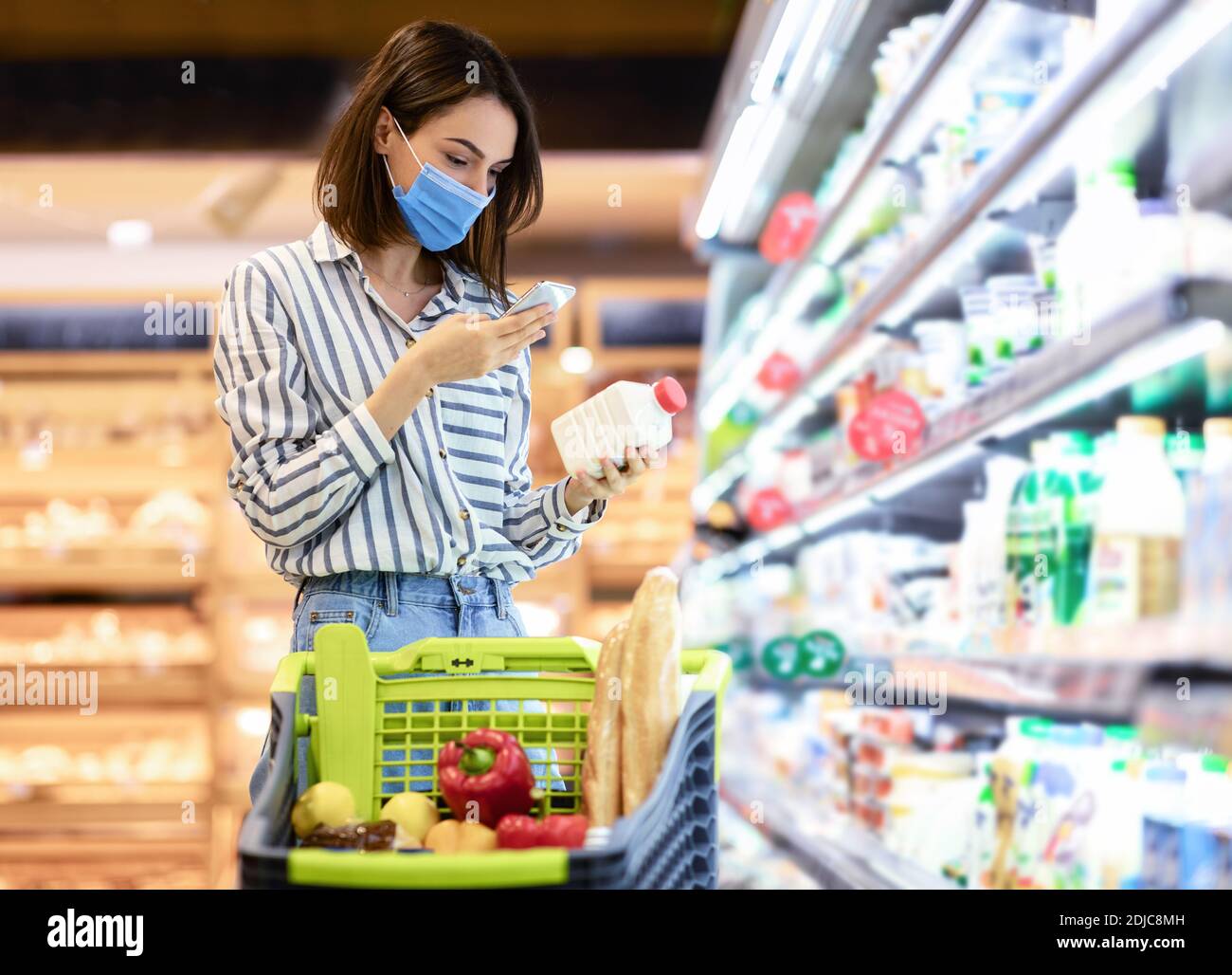 Frau in Maske Scannen Code auf Produkten mit Smartphone Stockfoto