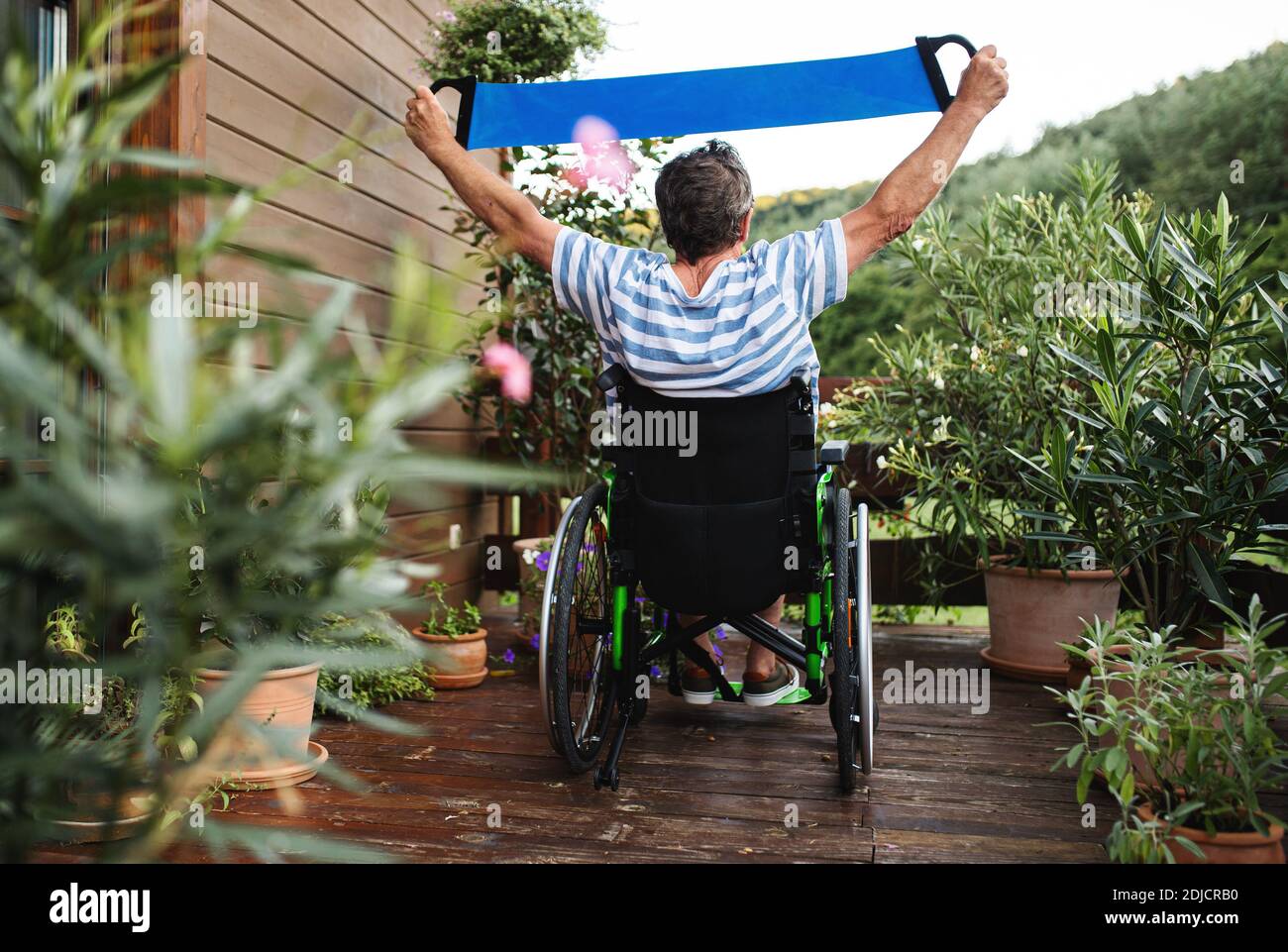 Rückansicht eines älteren Mannes im Rollstuhl, der auf der Terrasse trainieren kann. Stockfoto