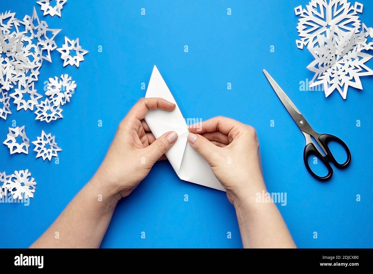 Hände machen weißes Papier Schneeflocken auf blauem Hintergrund Stockfoto