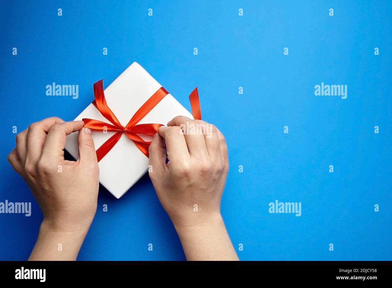Hände mit weißem Geschenkkarton mit rotem Band gebunden Blauer Hintergrund Stockfoto