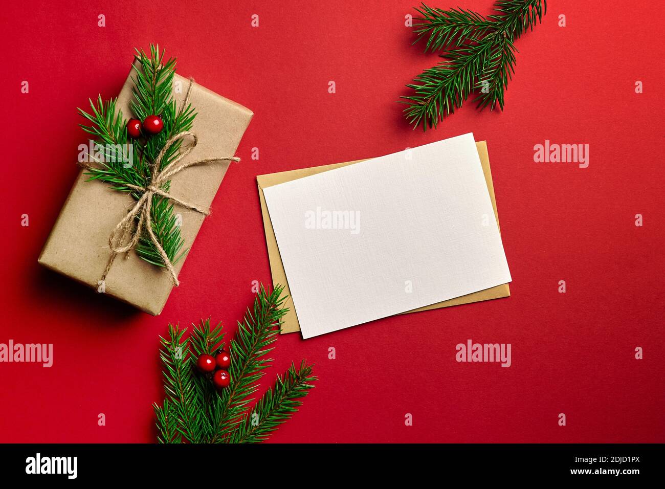 Weihnachten Grußkarte mockup. Dekorierte Geschenkbox mit Tannenzweig und Stechbeeren auf rotem Papierhintergrund. Draufsicht, Kopierbereich. Stockfoto