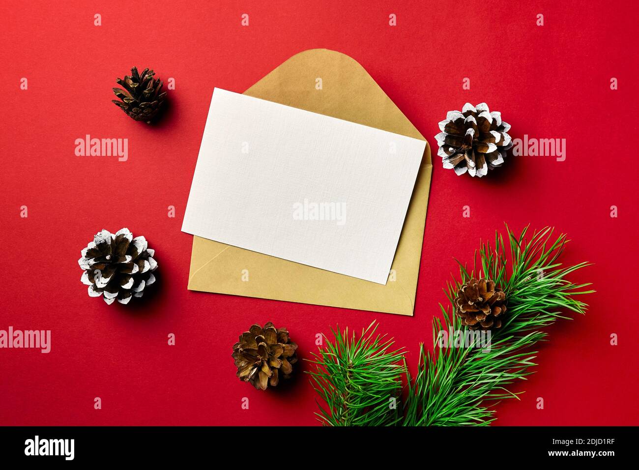 Weihnachten Grußkarte mockup. Karte mit Umschlag, Kiefernäste mit Zapfen auf rotem Papierhintergrund. Draufsicht, Kopierbereich. Stockfoto
