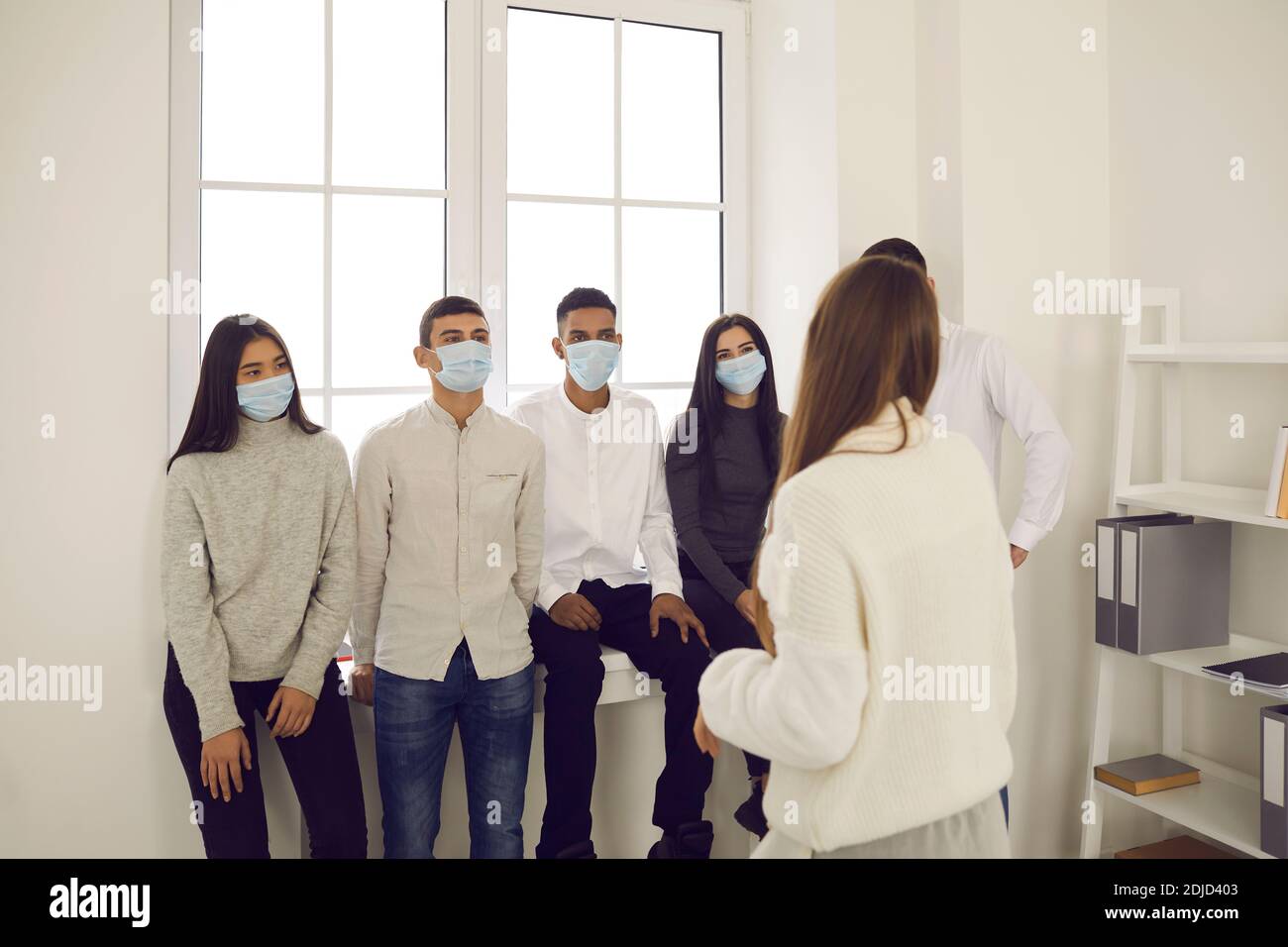 Gruppe von Büroangestellten in medizinischen Schutzmasken zuhören Präsentation einer Kollegin Stockfoto