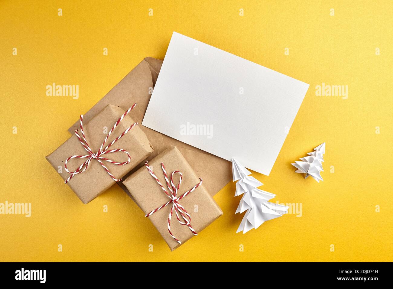 Grußkarte Mockup, weiße leere Wish Card mit Bastelpapierumschlag und Geschenkschachteln mit weißem Papier Fichte Baum auf goldenem Hintergrund. Leere Begrüßung Stockfoto