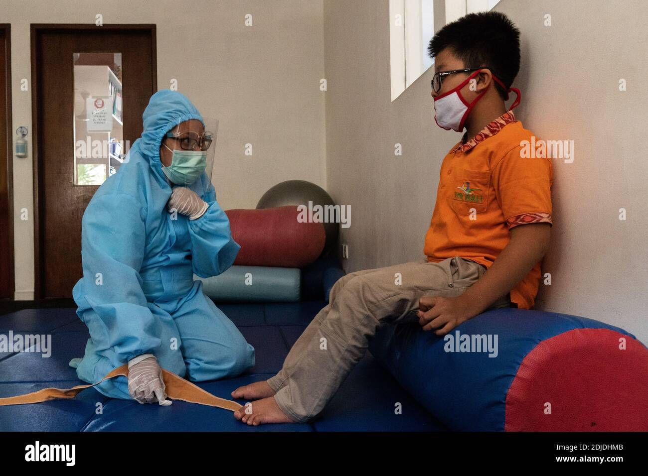 BALI/INDONESIEN-Okt 23 2020: Ein Kind mit einer körperlichen Behinderung macht eine Physiotherapie. Sie tragen Masken und Hamzat Anzug, um die Ausbreitung des C zu vermeiden Stockfoto