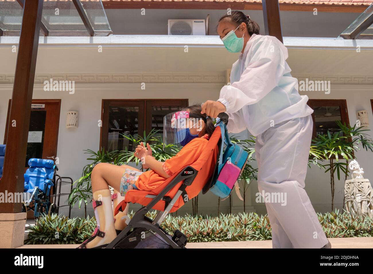 BALI/INDONESIEN-Okt 23 2020: Ein Kind mit einer körperlichen Behinderung macht eine Physiotherapie. Sie tragen Masken und Hamzat Anzug, um die Ausbreitung des C zu vermeiden Stockfoto