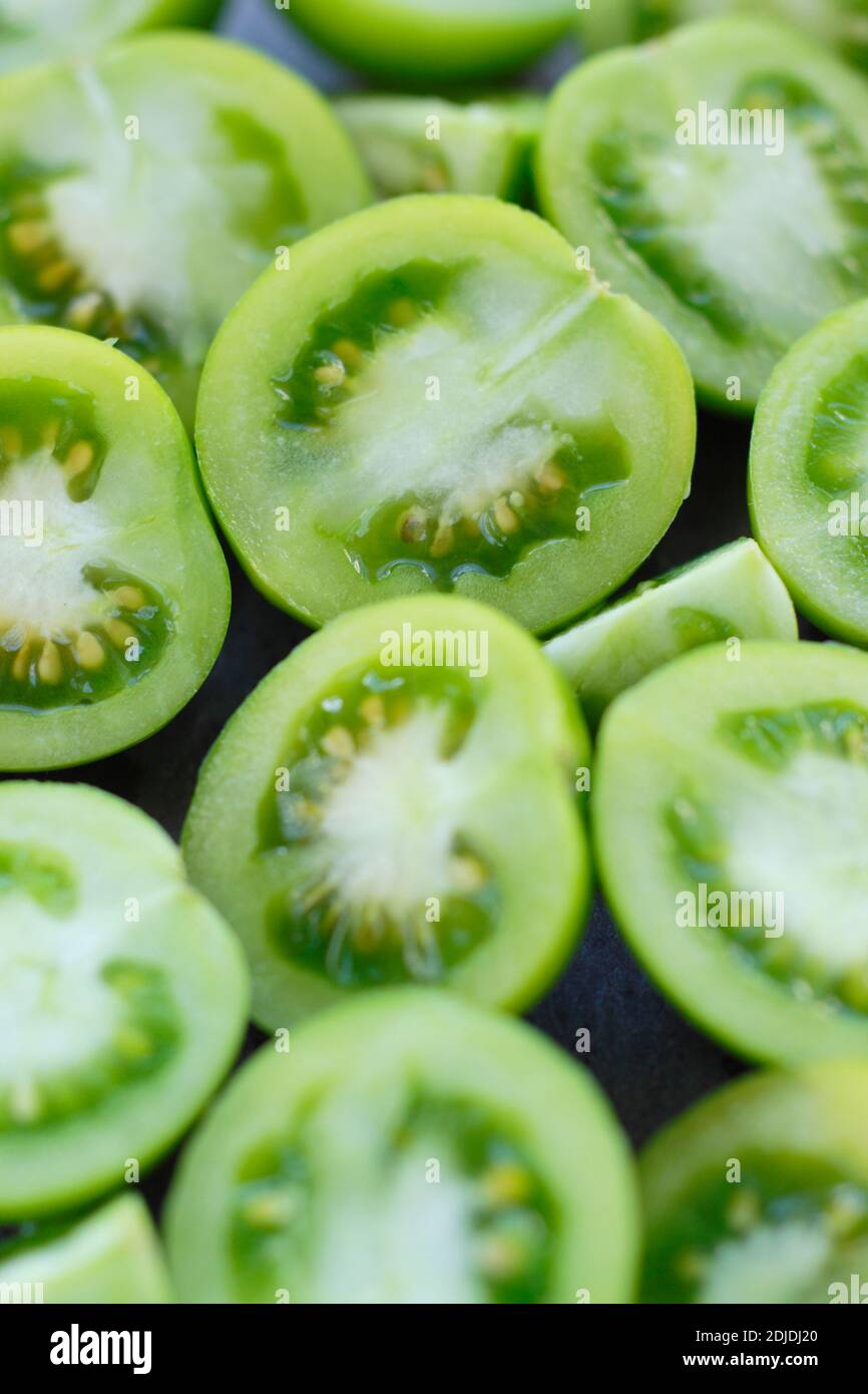 Solanum lycopersicum. Unreife grüne Tomaten in zwei Hälften auf Schieferplatte geschnitten. VEREINIGTES KÖNIGREICH Stockfoto