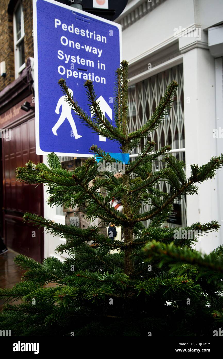 London Dezember 2020. Columbia Road, Tower Hamlets. Sonntäglicher Blumenmarkt. Ein Weihnachtsbaum vor einem Schild, das einbahnt, um mit Co. Zu entsprechen Stockfoto