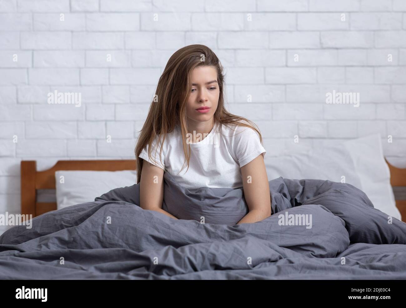 Junge Frau, die allein in ihrem Bett sitzt, in den Weltraum starrt und an einer klinischen Depression leidet Stockfoto