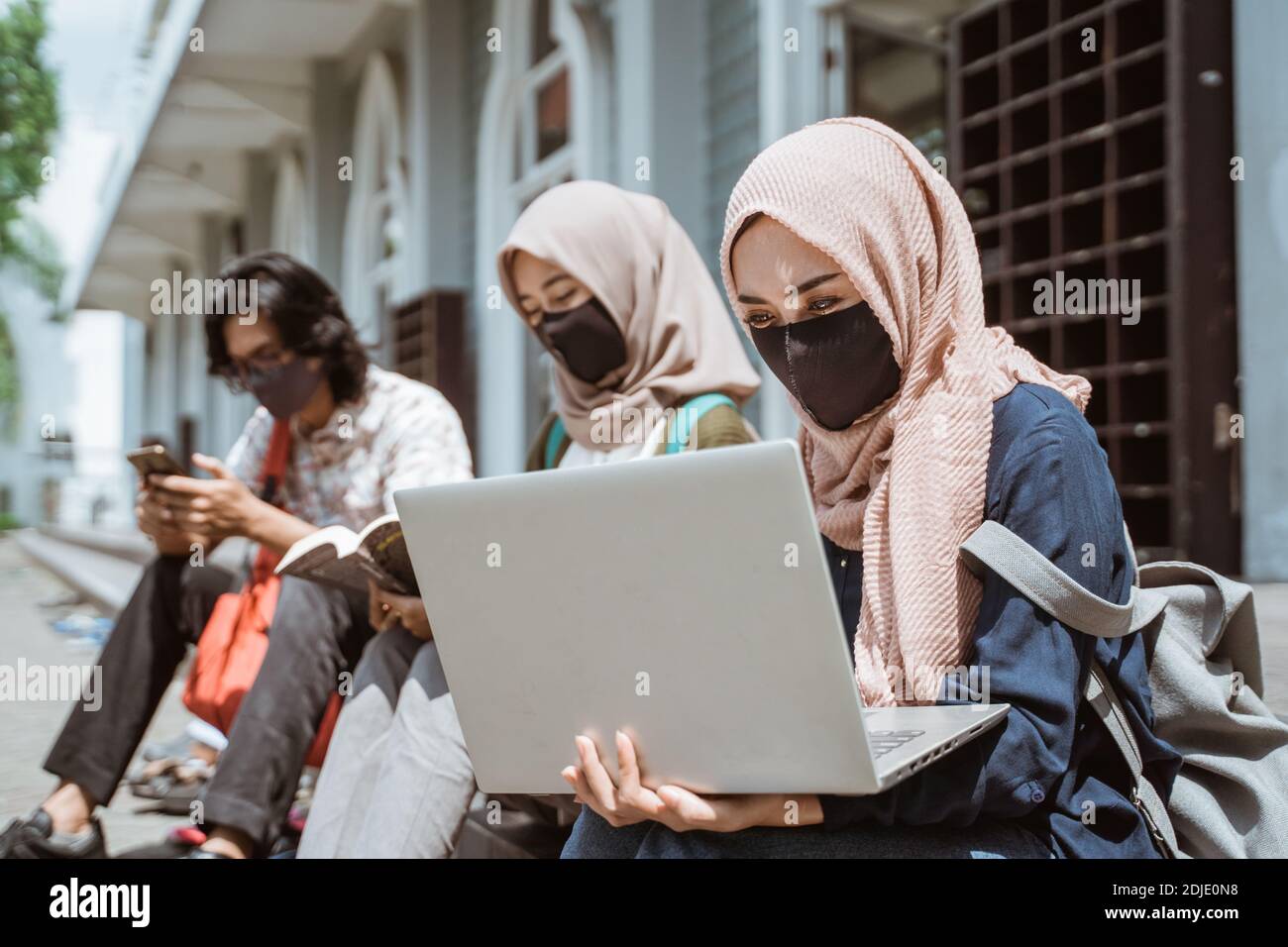Portrait muslim trägt Masken Schülerinnen, die damit beschäftigt sind, ihre Aufgaben auf einem Laptop. Mit Freunden im Hintergrund Stockfoto