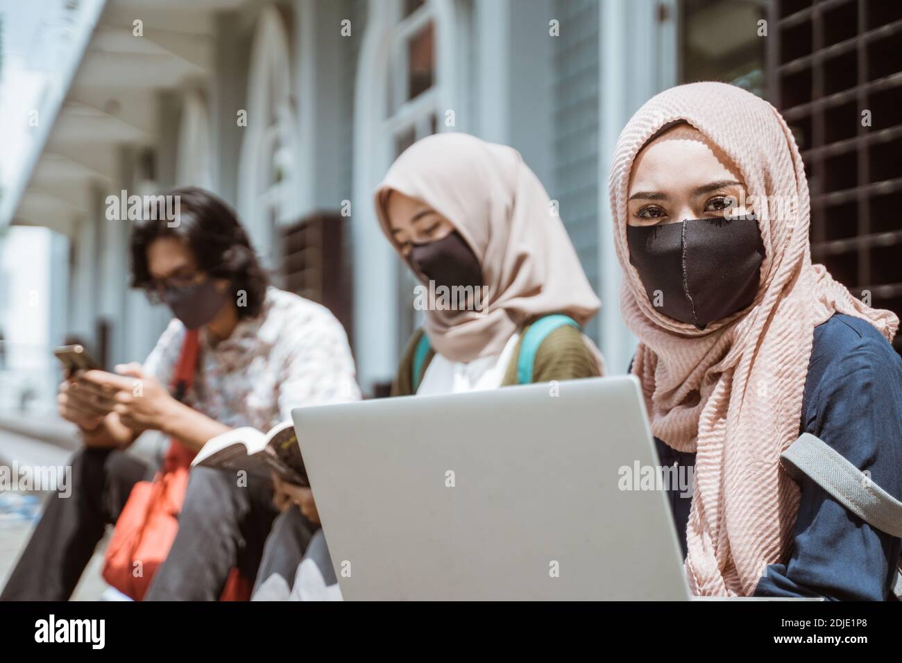 Portrait muslim trägt Masken Studentinnen, die auf die Kamera schauen. Mit fleißigen Freunden im Hintergrund Stockfoto