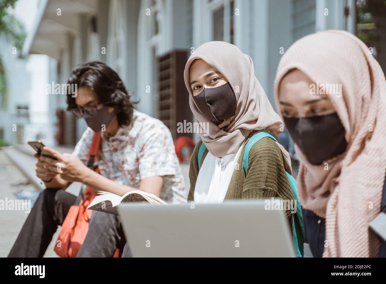 Portrait muslim trägt Masken Studentinnen, die auf die Kamera schauen. Mit fleißigen Freunden im Hintergrund Stockfoto