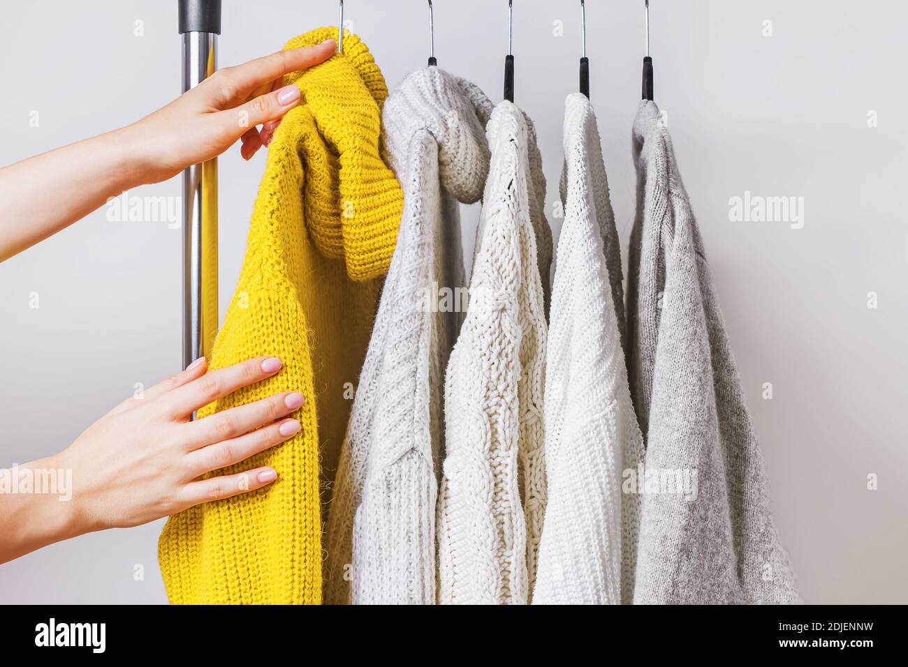 Die Frau Hände Wahl gelb Strickpullover unter anderem auf Kleiderbügel Stockfoto