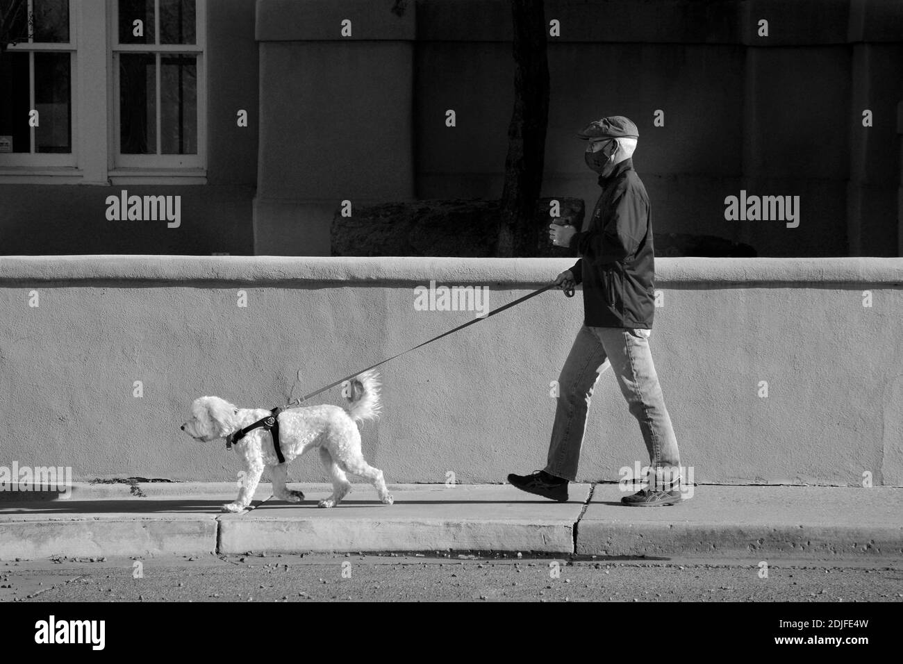 Ein Mann mit einer covid-19 Pandemiemaske geht mit seinem Hund auf einem Bürgersteig in Santa Fe, New Mexico. Stockfoto