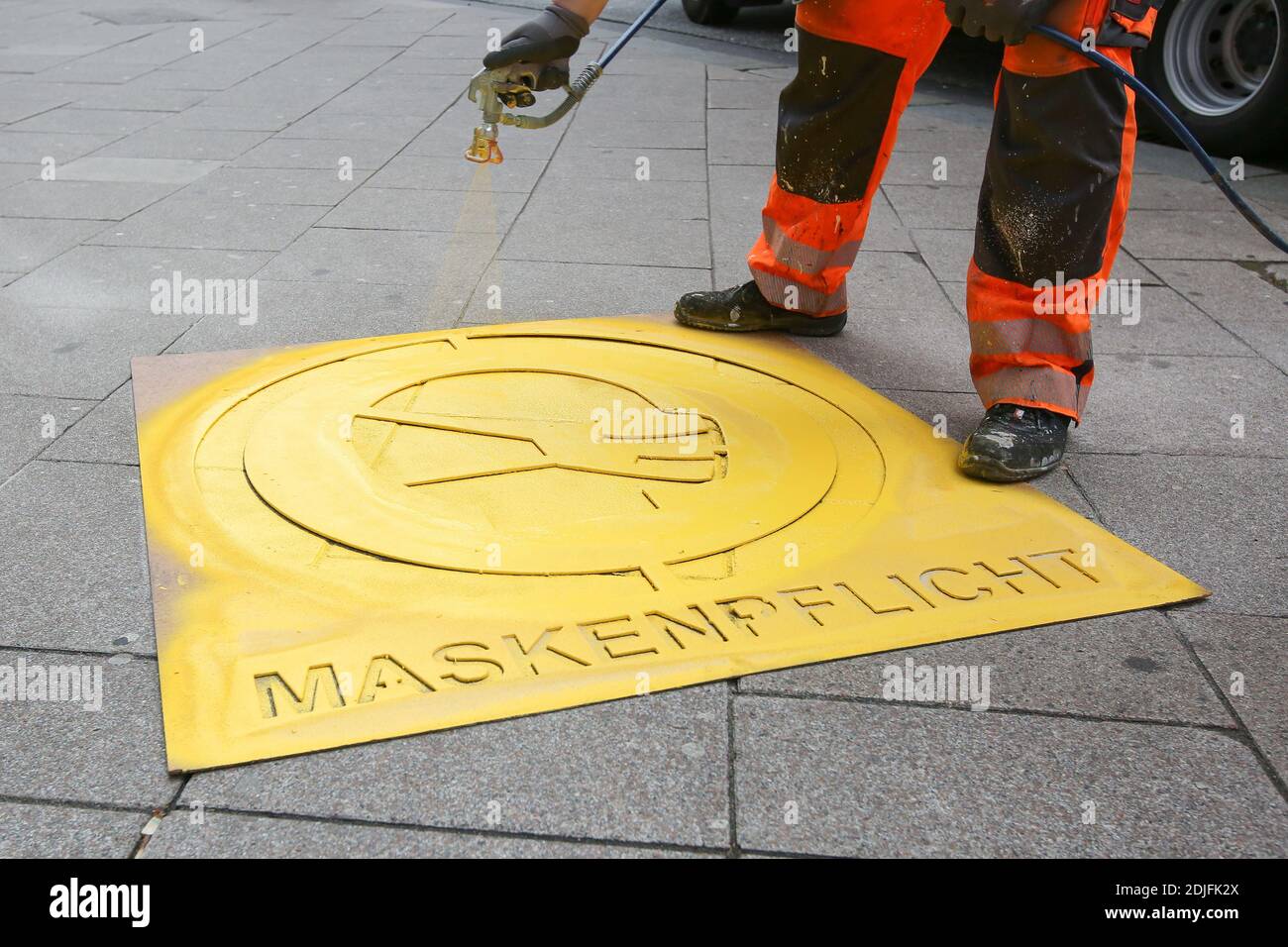 Hamburg, Deutschland. Dezember 2020. Mit einer Schablone und gelber Farbe setzen die Arbeiter ein Piktogramm und einen Hinweis auf einen Bürgersteig im Hamburger Einkaufszentrum Mönckebergstraße, um darauf hinzuweisen, dass Masken Pflicht sind. Kredit: Bodo Marks/dpa/Alamy Live Nachrichten Stockfoto