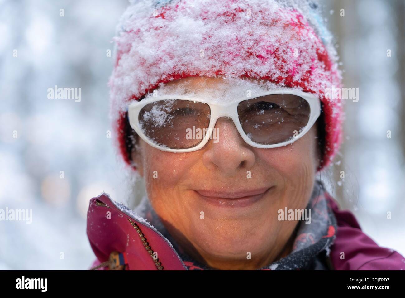 Nahaufnahme Porträt einer hübschen zeitlosen älteren Frau im Winterwald, stehend unter fallendem Schnee. Sorglose Frau genießt Schnee und Winter Zeit. Sie pl Stockfoto