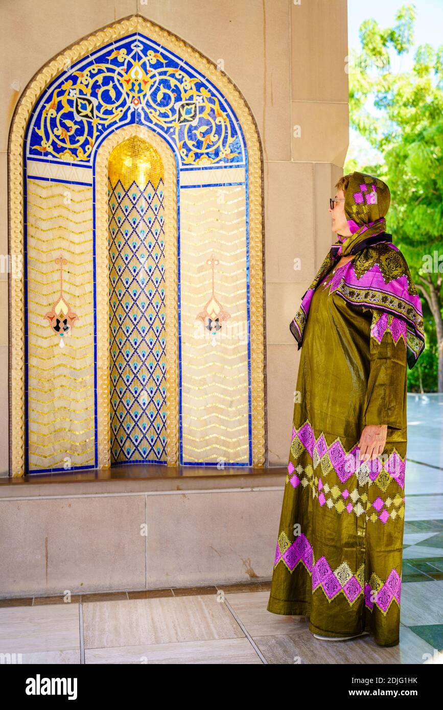 Eine Frau, die in einem traditionellen omanischen Abaya gekleidet ist und eine verzierte Nische in der Sultan Qaboos Moschee in Muscat, Oman, betrachtet Stockfoto