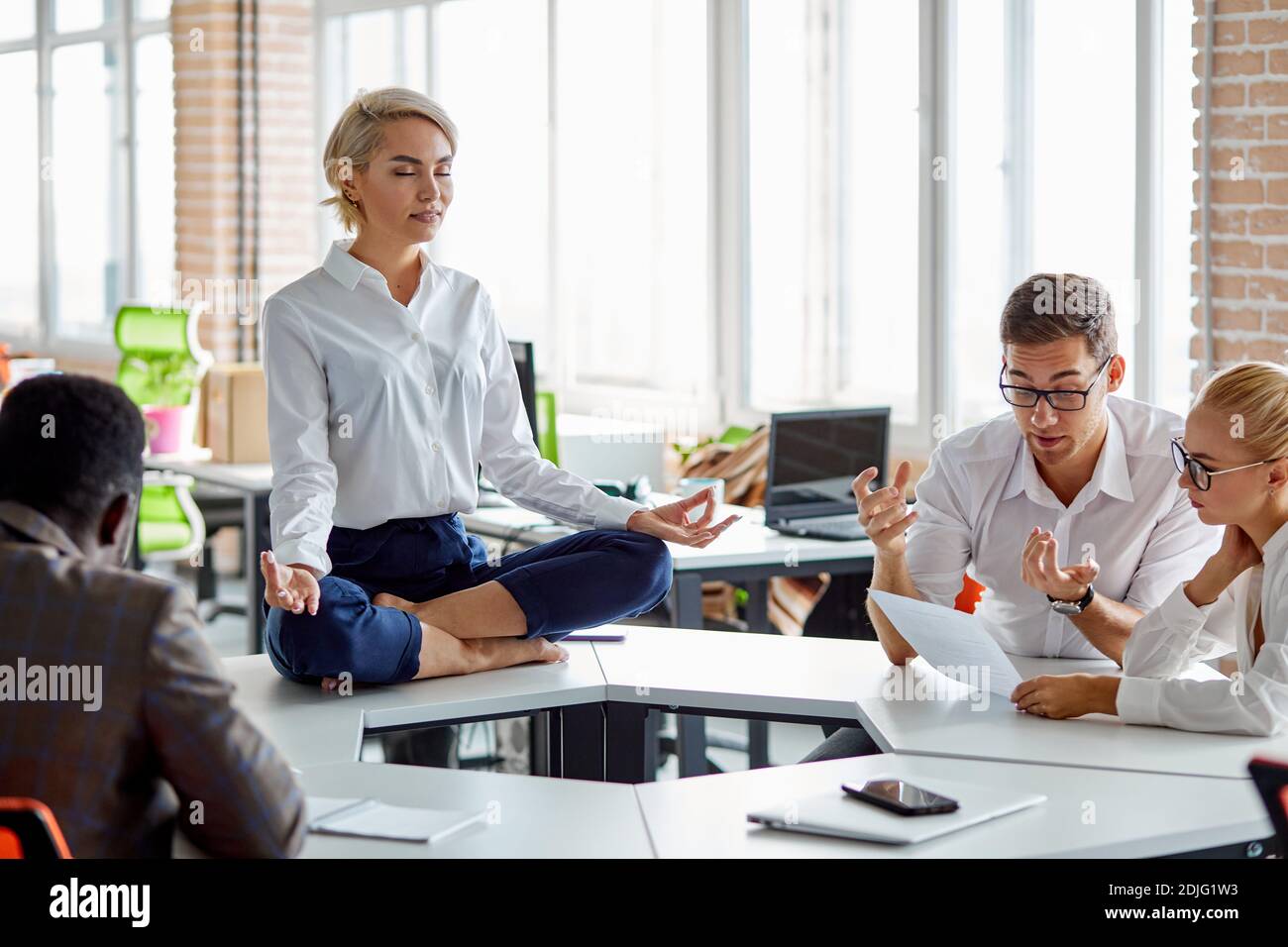 Gestresste Frau bei der Arbeit ruhig zu halten, Gleichgewicht der psychischen und psychischen Gesundheit zu halten, sitzt meditierend während Brainstorming, auf dem Tisch Stockfoto