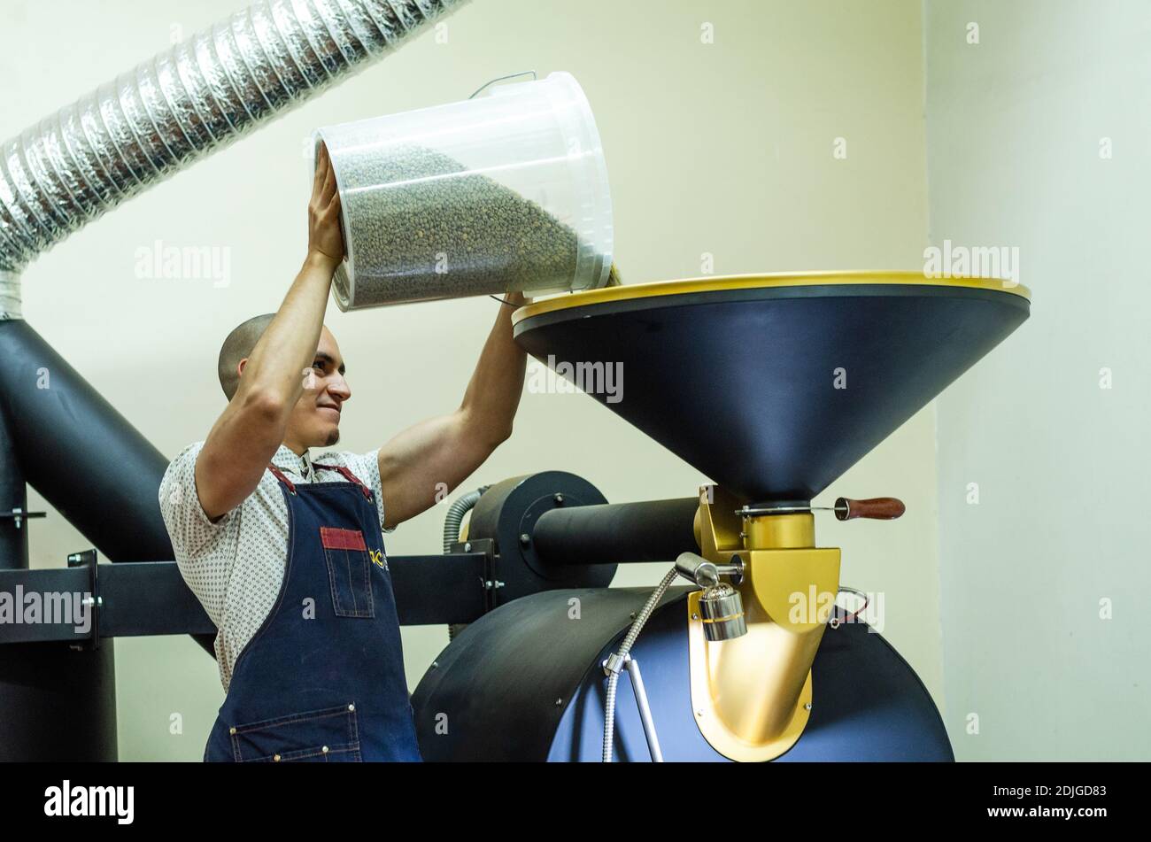 Mann gießt rohe Kaffeebohnen in eine Kaffeeröstermaschine Stockfoto