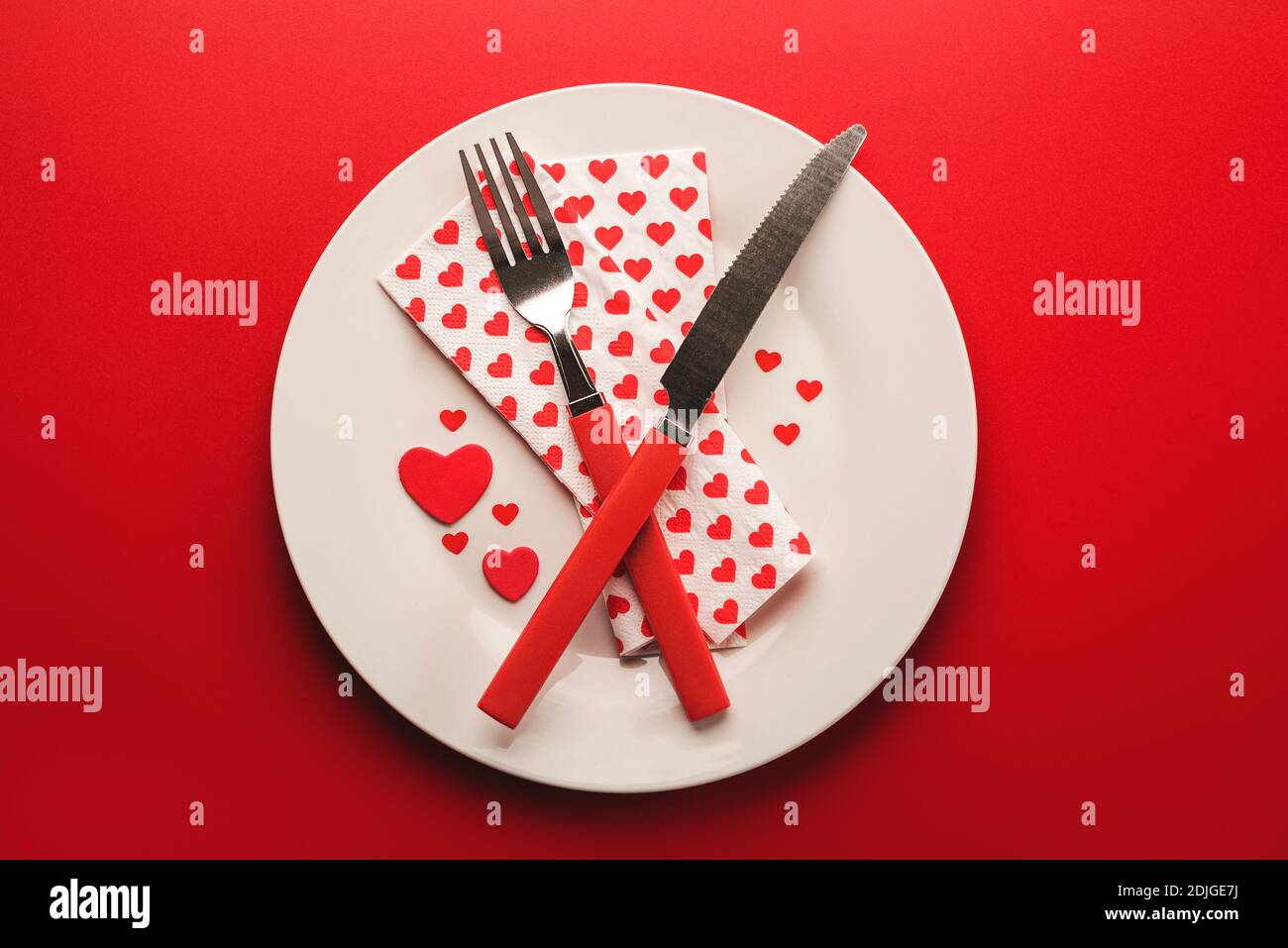 Alles Liebe zum Valentinstag.Rotes Besteck serviert auf dem Teller für Valentinstag Auf rotem Hintergrund .Valentines Tag Dinner Konzept Stockfoto