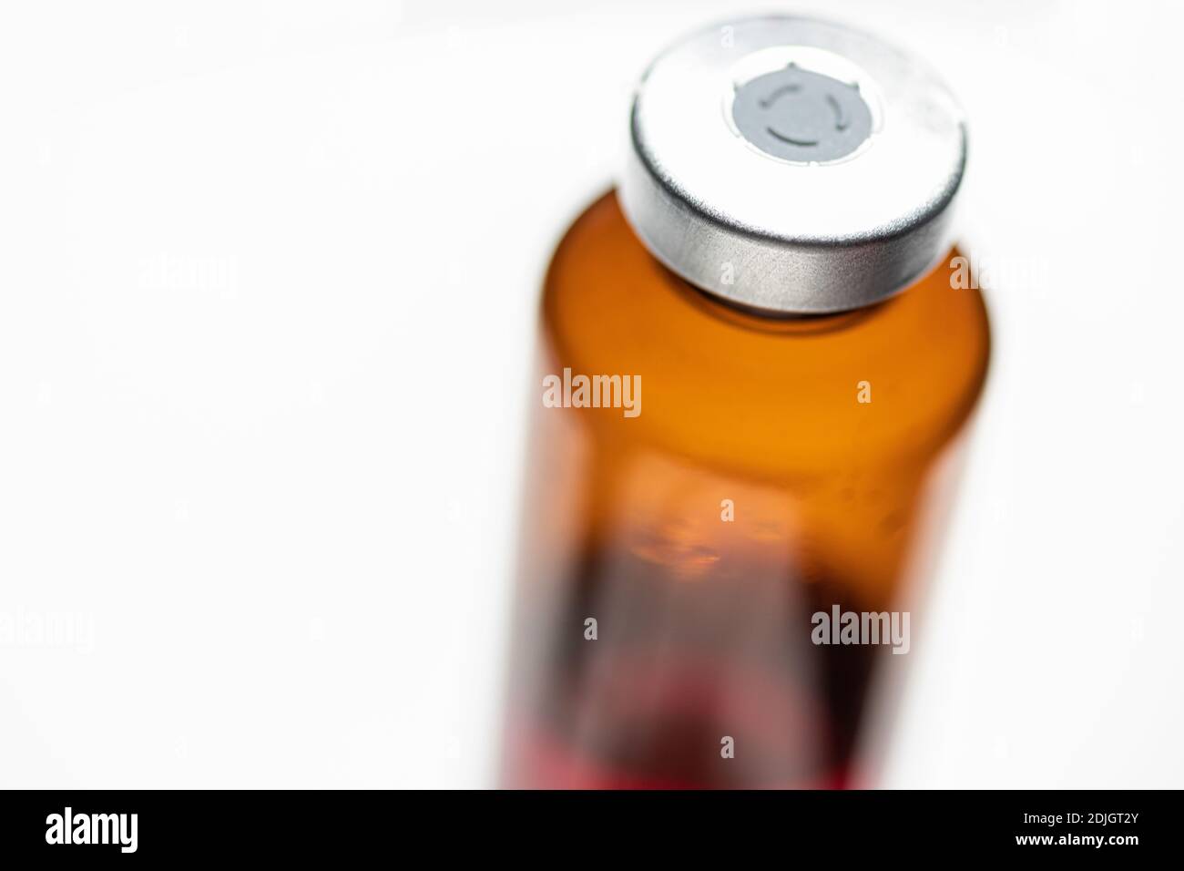 Eine Makroaufnahme mit selektivem Fokus einer bernsteinfarbenen Impfstoffflasche auf weißem Hintergrund. Stockfoto