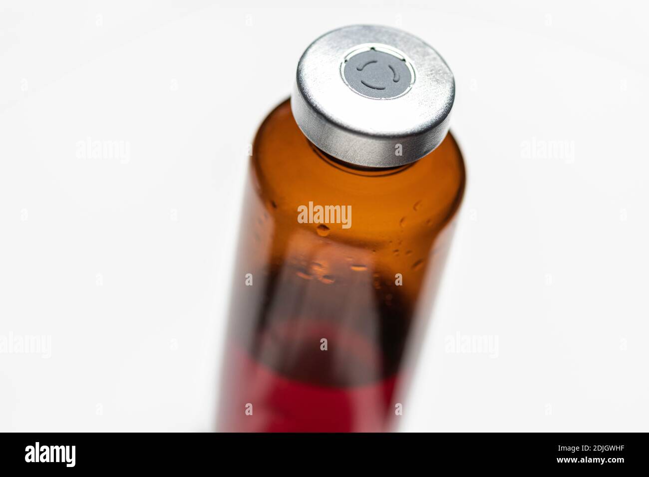Eine Makroaufnahme mit selektivem Fokus einer bernsteinfarbenen Impfstoffflasche auf weißem Hintergrund. Stockfoto