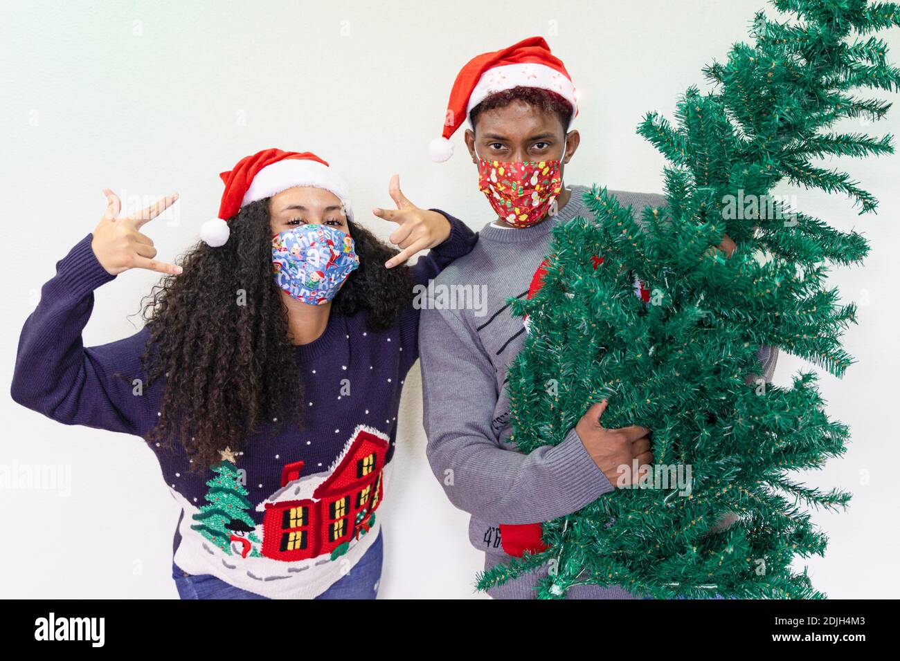 Rockpaar. Freund mit einem weihnachtsbaum Gitarre und attraktive junge Frau macht Horn Zeichen Hand Geste mit Schutzmasken . Weihnachten und ne Stockfoto