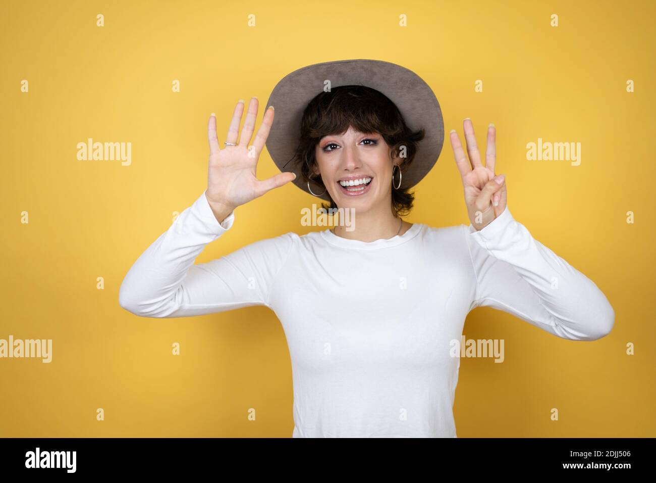 Junge kaukasische Frau trägt Hut über isolierten gelben Hintergrund zeigt Und mit den Fingern Nummer acht nach oben zeigen und dabei selbstbewusst lächeln Und glücklich Stockfoto