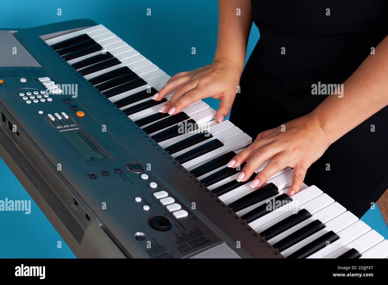 Nahaufnahme von weiblichen Händen und Fingern einer Frau, die einen elektronischen Synthesizer spielt, isoliert auf einem blauen Hintergrund Stockfoto