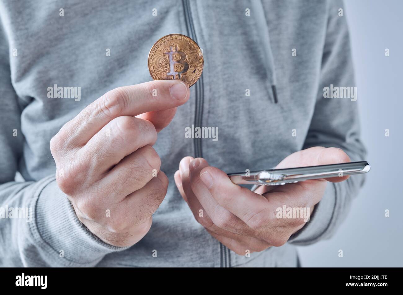 Bitcoin Trading App für Smartphones, konzeptionelles Bild, Mann hält Kryptowährung Münze und Handy in Händen. Stockfoto