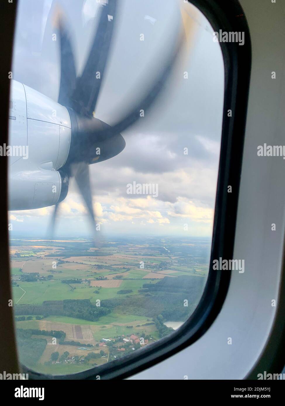 Blick aus dem Flugzeugfenster auf Felder, Wiesen, Wälder und den rotierenden Propeller einer Turbo-Prop-Maschine Stockfoto
