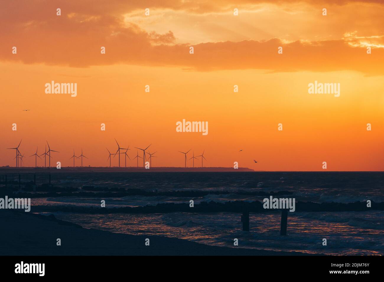 Windturbinen-Stromerzeuger Silhouetten an der Meeresküste bei Sonnenuntergang. Alternative Erzeugung erneuerbarer Energien. Stockfoto