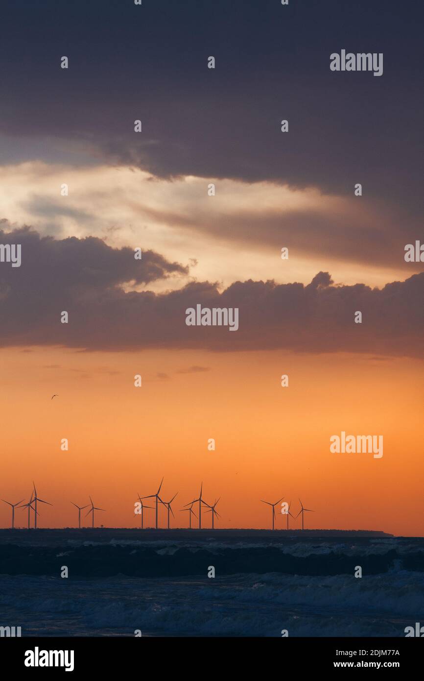 Windturbinen-Stromerzeuger Silhouetten an der Meeresküste bei Sonnenuntergang. Alternative Erzeugung erneuerbarer Energien. Stockfoto