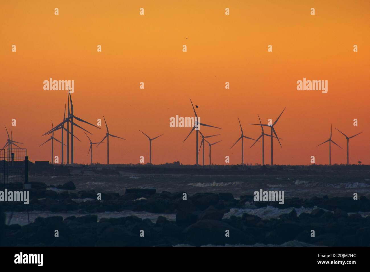 Windturbinen-Stromerzeuger Silhouetten an der Meeresküste bei Sonnenuntergang. Alternative Erzeugung erneuerbarer Energien. Stockfoto