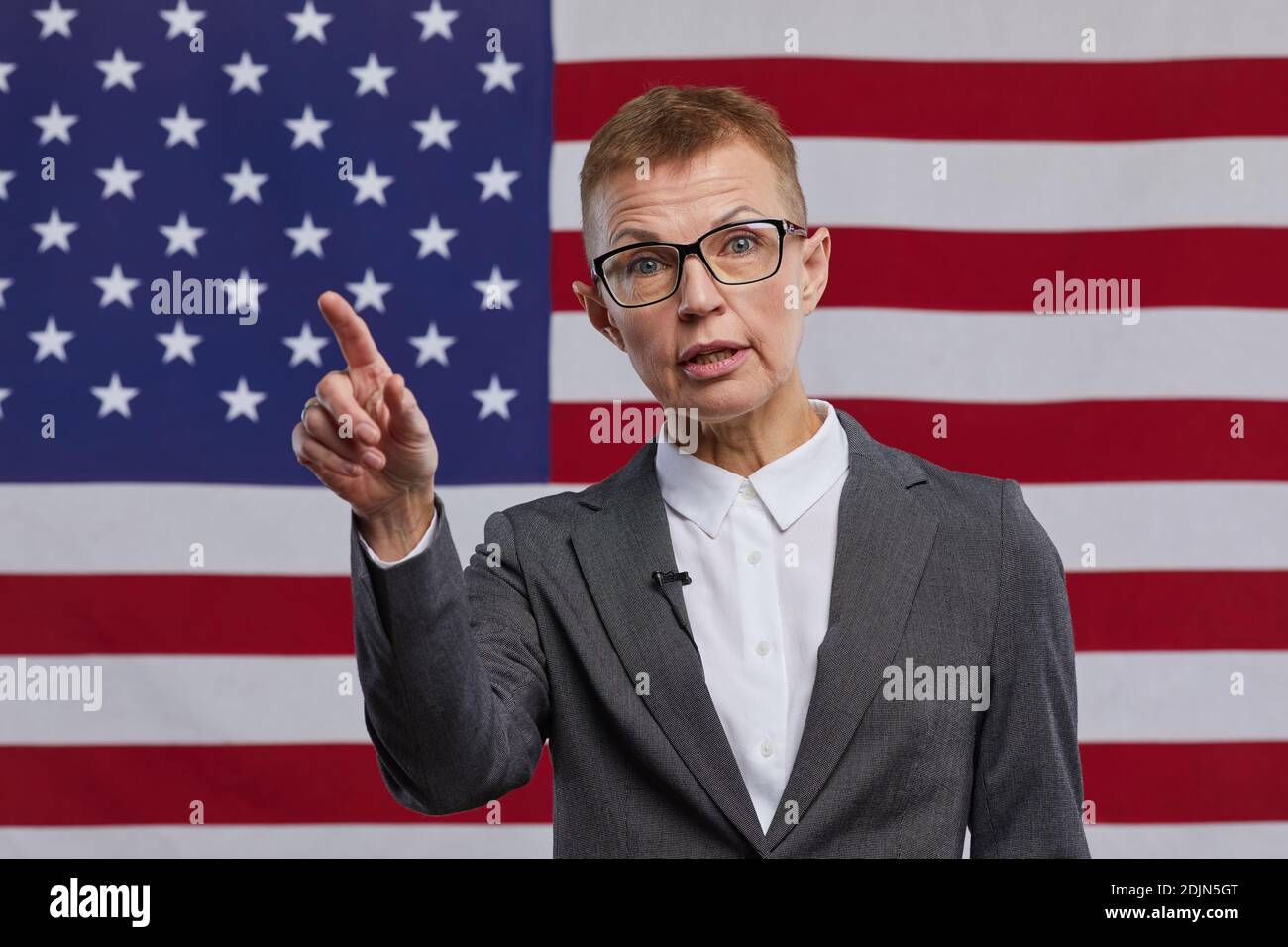 Vorderansicht Porträt einer reifen Politikerin, die Rede hält und gestikiert, während sie vor dem Hintergrund der US-Flagge steht, Kopierraum Stockfoto