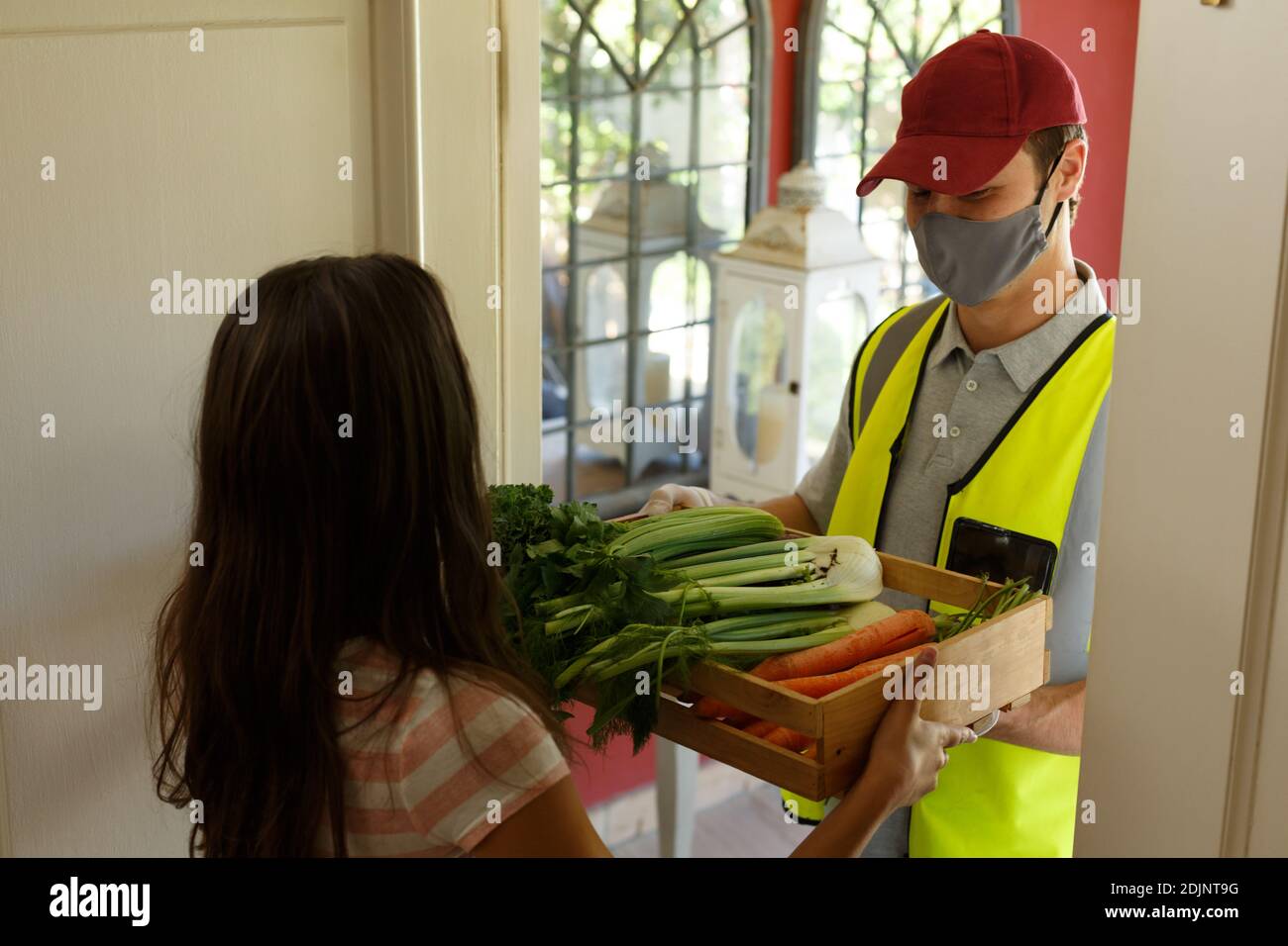 Kaukasische Frau, die Lebensmittel-Box aus Lieferung Mann trägt Gesicht Maske an der Vordertür Stockfoto