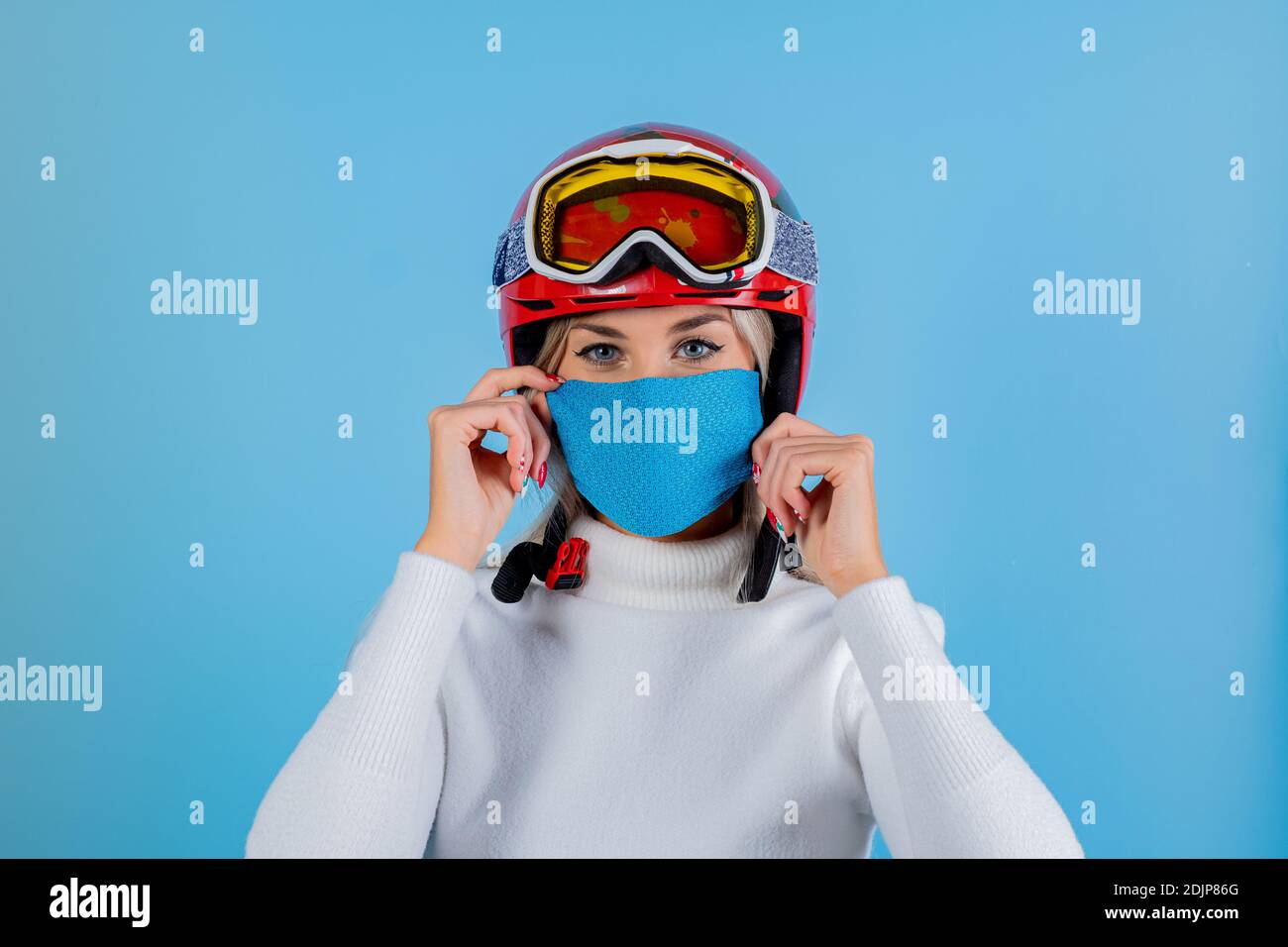 Nahaufnahme Porträt eines Mädchen Skifahrer trägt eine leichte blu Schutzmaske, Helm und Brille. Ein Snowboarder auf hellem blu-Hintergrund. Covid19 Coronavir Stockfoto