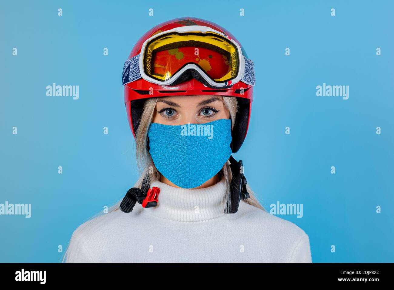 Nahaufnahme Porträt eines Mädchen Skifahrer trägt eine leichte blu Schutzmaske, Helm und Brille. Ein Snowboarder auf hellem blu-Hintergrund. Covid19 Coronavir Stockfoto
