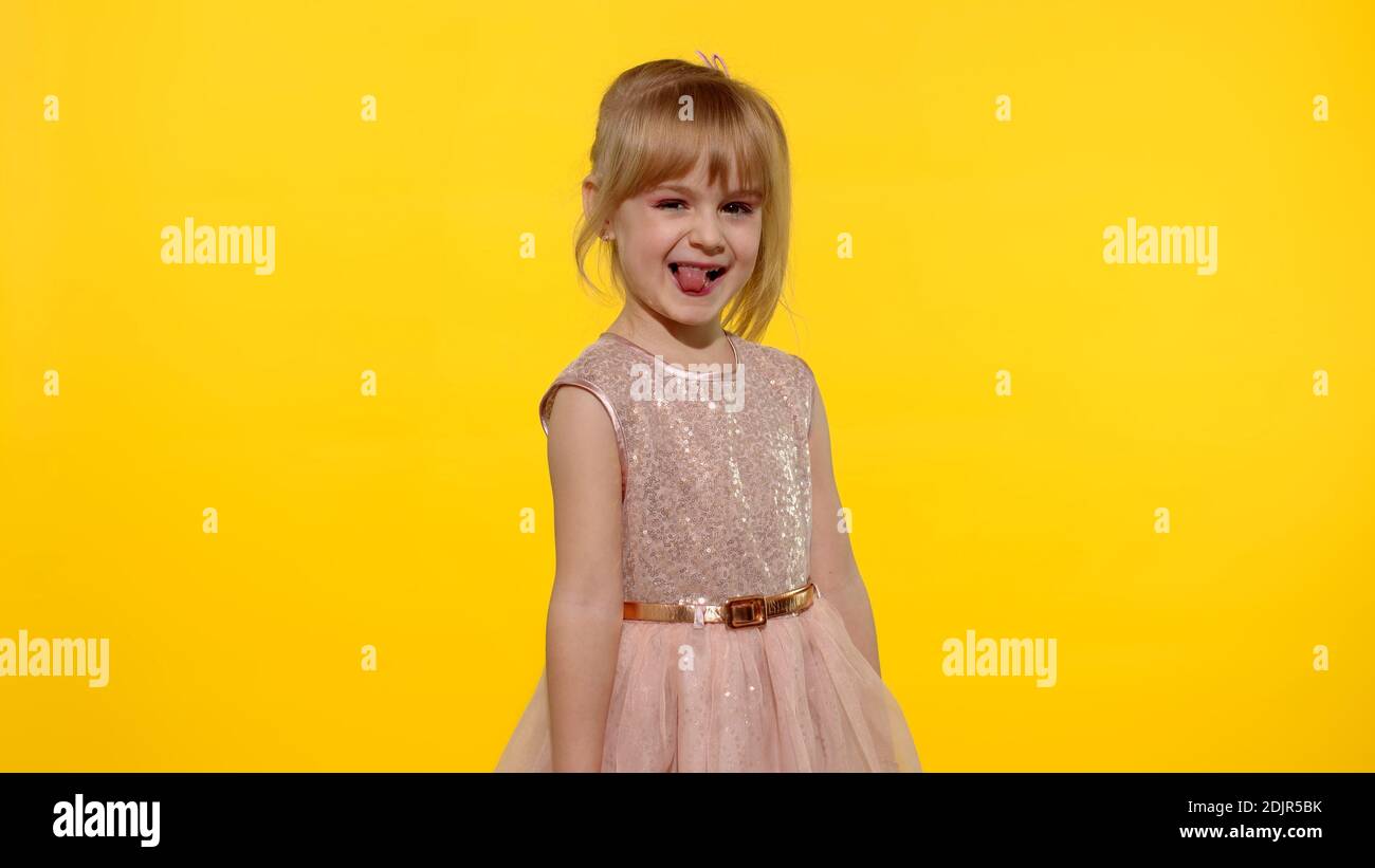 Kleine blonde Teenager-Kind Mädchen 5-6 Jahre alt in rosa Kleid posiert isoliert auf gelbem Hintergrund Studio. Menschen Emotionen Konzept. Kind lachend, herumtörnend, Zunge zeigend Stockfoto