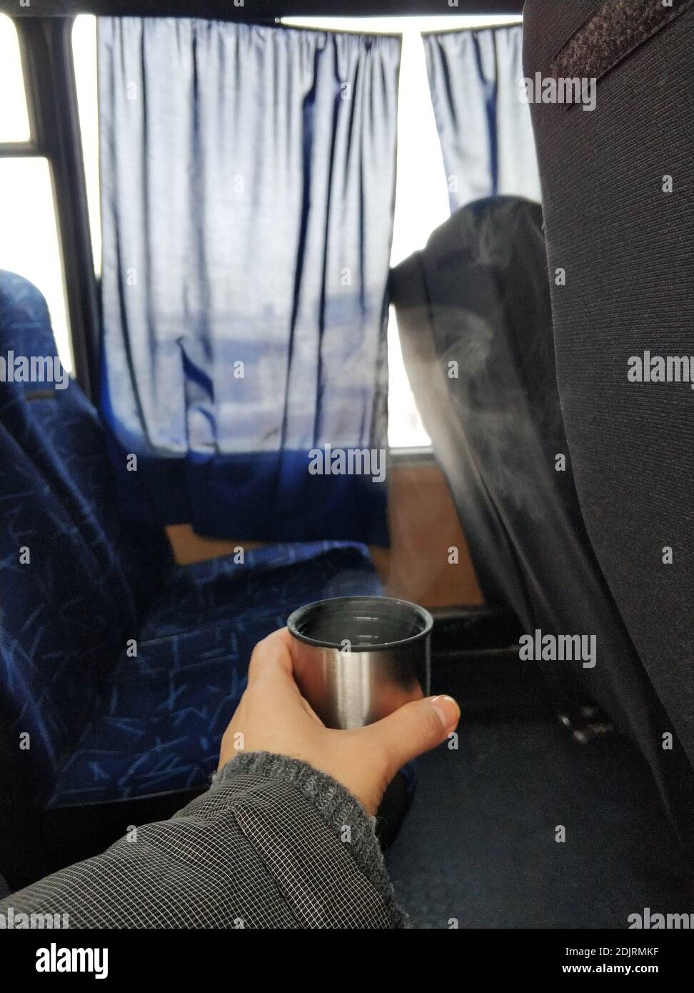 Ein Mann hält in der Hand eine Kappe aus einer Thermoskanne mit dampfendem heißen Tee, in der Kabine des Busses. Heißes Getränk während der Reise. Stockfoto