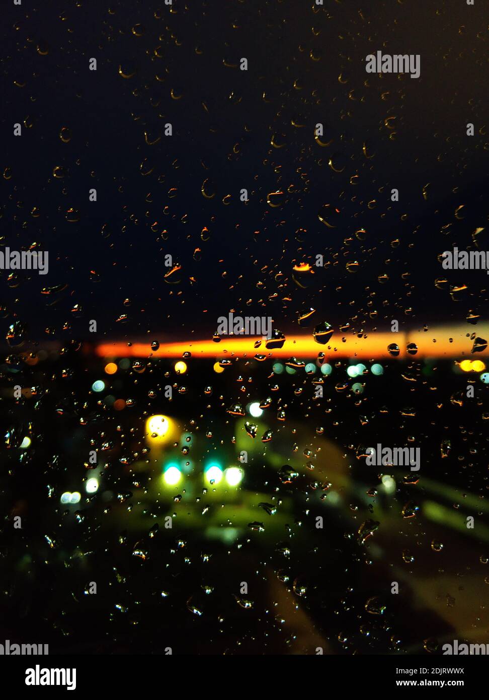 Regentropfen auf Glas. Livin bei Sonnenuntergang. Nachthimmel mit einem leuchtend orangefarbenen Streifen. Stockfoto