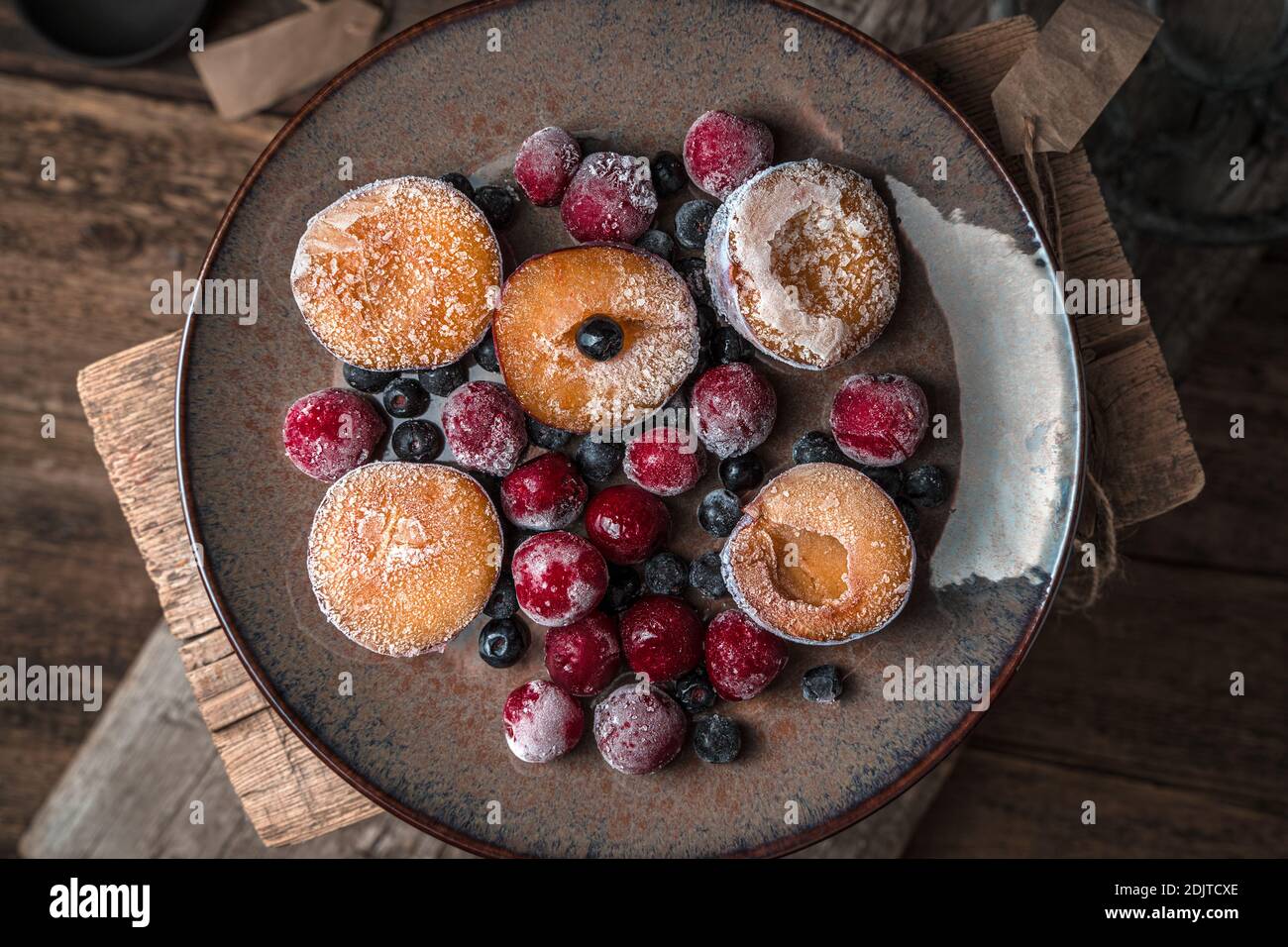 Verschiedene gefrorene Beeren und Früchte in einem braunen Teller auf einem hölzernen Hintergrund. Stockfoto