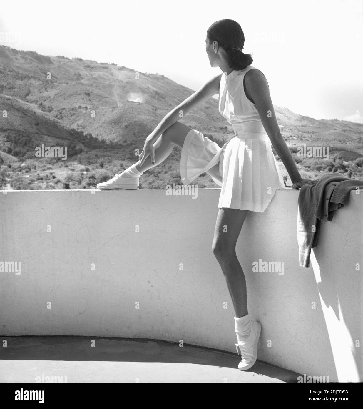 Fashion Model trägt Tennis Outfit, Ganzkörperportrait sitzt an der Wand mit Bergen im Hintergrund, Foto von Toni Frisell, Februar 1947 Stockfoto
